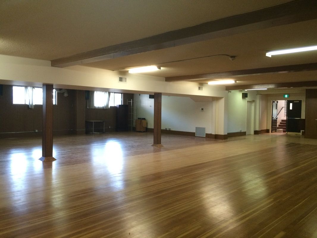 The Downstairs Hall, an open wooden-floored room with windows along one wall