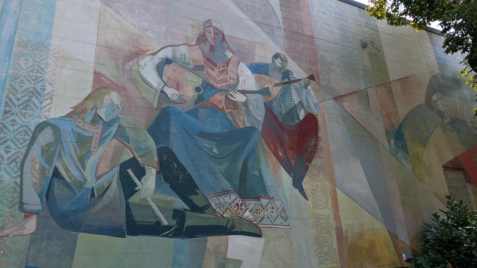 The mural on the Russian Hall's outside wall: musicians in folk dress playing stringed instruments, painted in soft blues, rose and ochre